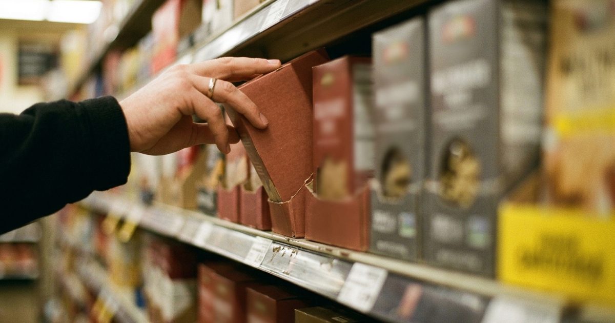 Mano tomando un producto envasado de la góndola de un supermercado
