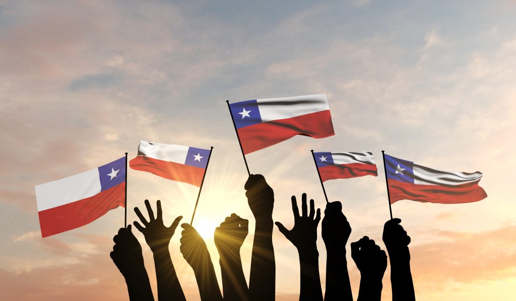 Personas levantando banderas de Chile al atardecer durante la celebración de Fiestas Patrias, simbolizando orgullo y unión nacional.